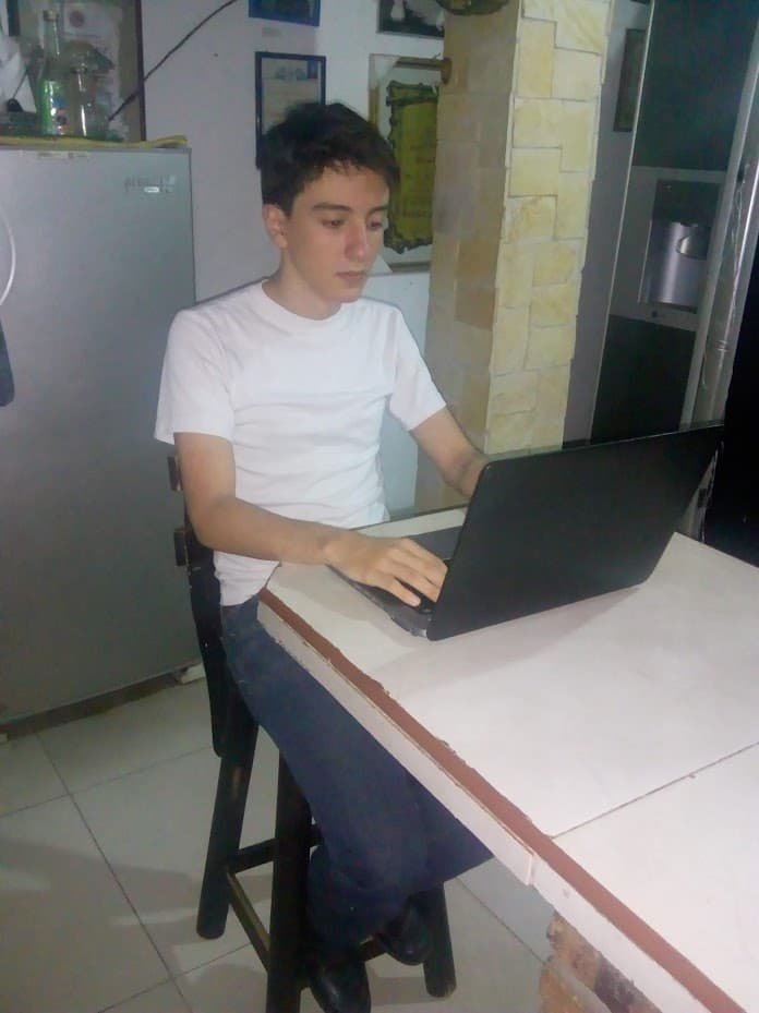Yo, más joven, con una camiseta blanca en el mesón de la cocina, encorvado sobre una laptop, escribiendo.