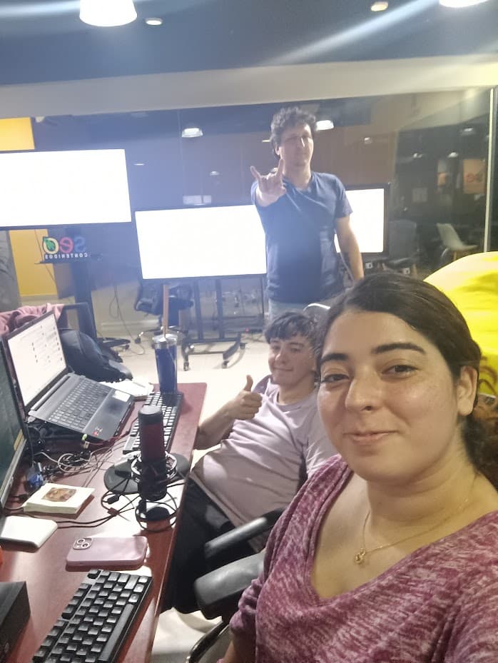 Tres de nosotros en esa misma oficina, en plena jornada, con monitores y un micrófono sobre los escritorios y el logo de la empresa detrás.