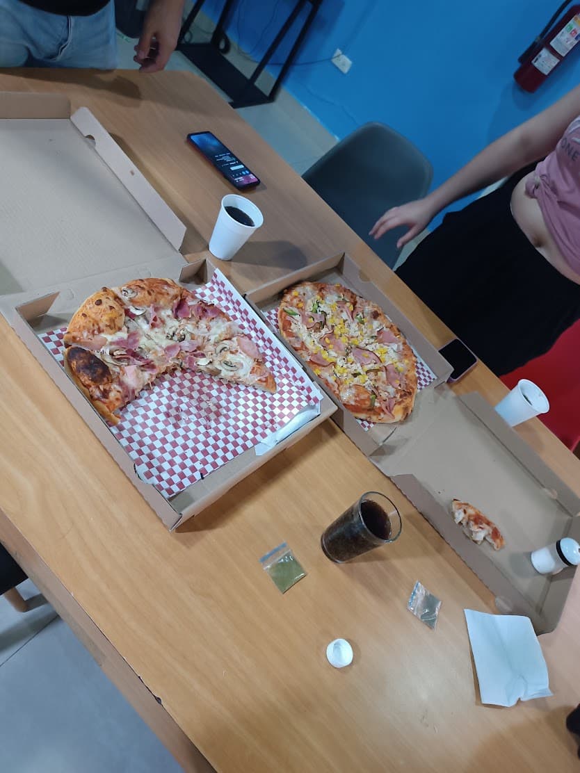 Dos cajas de pizza abiertas sobre una mesa de reuniones, con vasos, un teléfono y el equipo alrededor.