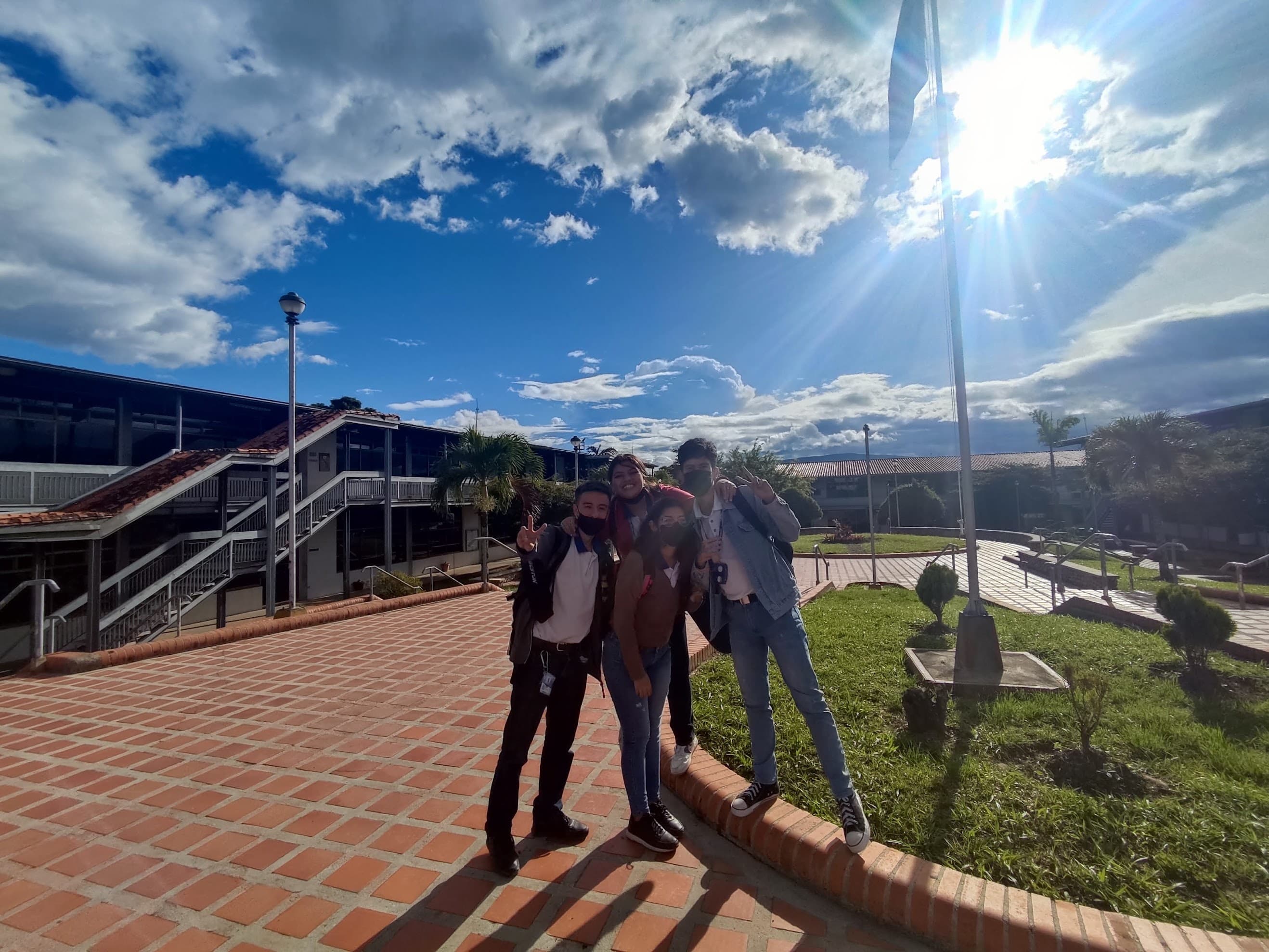 Cuatro de nosotros posando afuera del campus de la UNEFA en un día despejado, todavía con tapabocas, con el asta de bandera y los pasillos detrás.